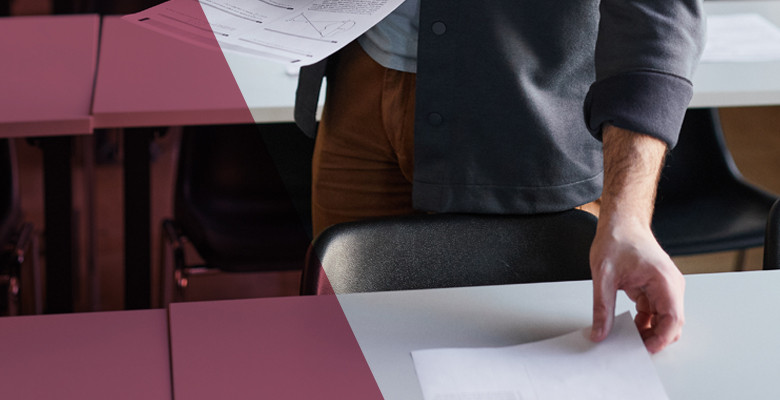 Ein Symbolbild zeigt eine Lehrperson beim Einsammeln von Heften.